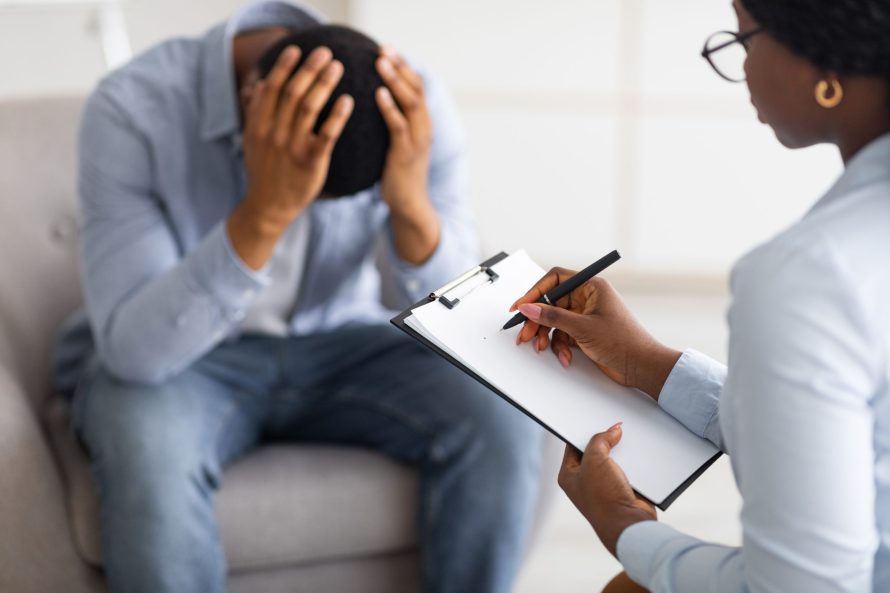 Depressed black guy holding his head at counselor’s office, seeking professional help with mental disorder