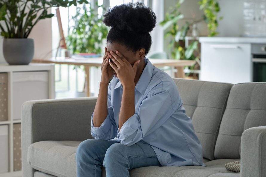 Depressed exhausted unhappy young woman sits on home couch hiding face in hands feel cheated alone.